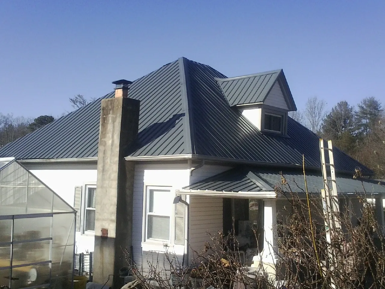 Dark blue standing seam metal roof on a white farmhouse with dormer — Slate & Tile Roof Repair by Roofing Brothers in Kyle