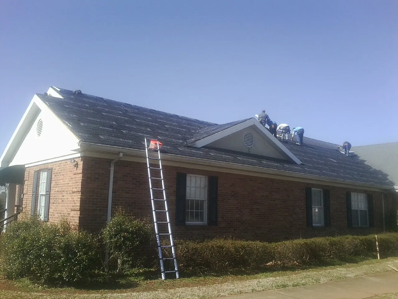 Crew tearing shingles off a brick ranch roof with a ladder set — Emergency Roof Repair work by our crew in Kyle