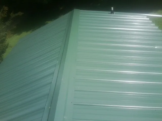 New green metal panels meeting at the ridge of a roof — Flat Roof Repair work by our crew in Kyle