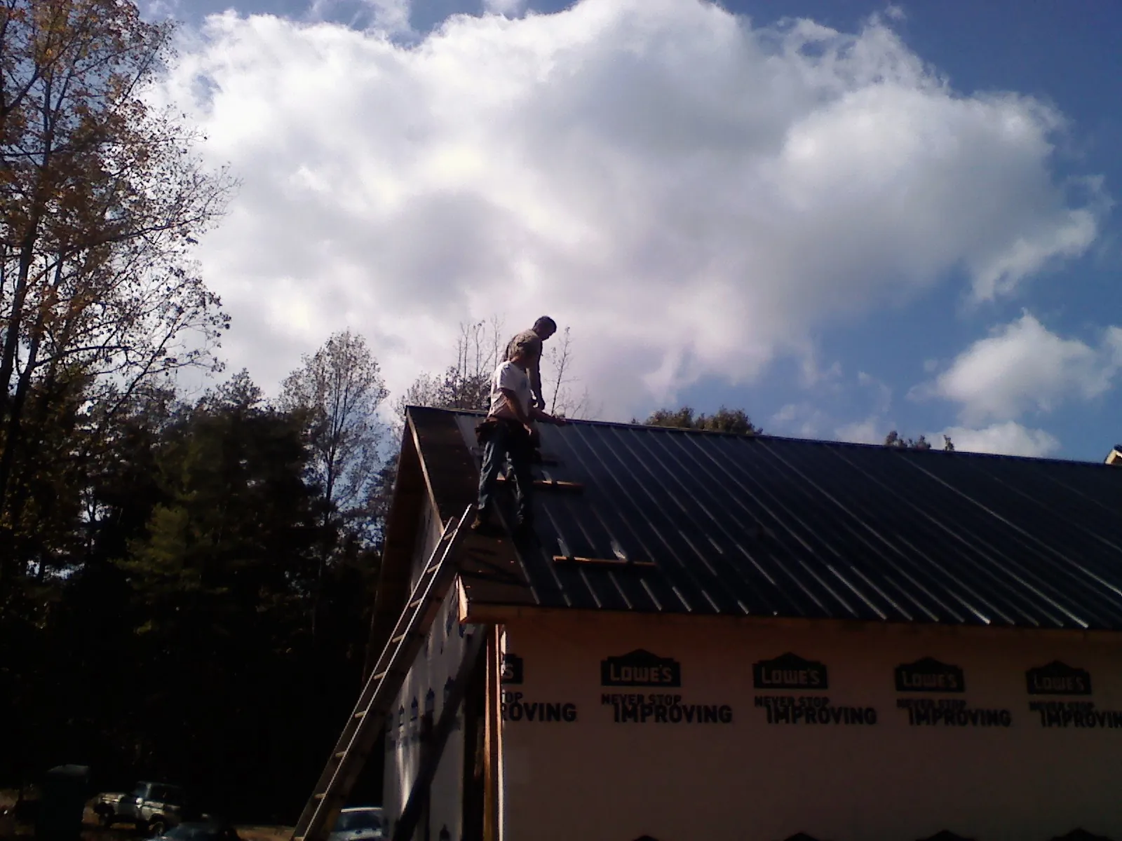 Roofer fastening dark metal panels high against a cloudy sky, from a Roof Inspection job in Kyle
