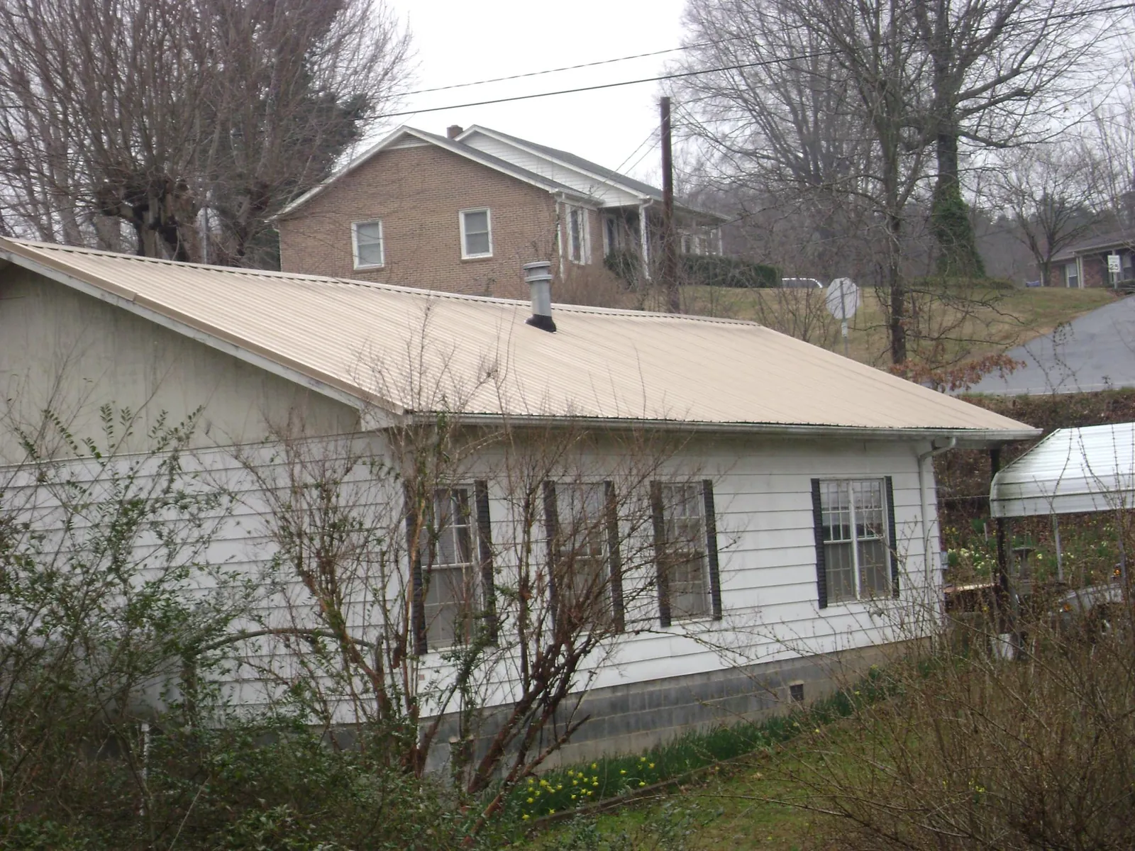 Tan metal roof on a white sided house set into a hillside — Commercial Roofing by Roofing Brothers in Kyle